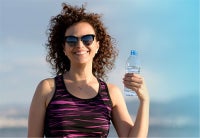 Young athletic lady holding a water bottle with sky in the background.